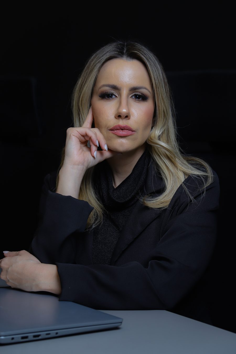 Ana Mascarenhas sentada à mesa, olhar direto para a câmera, em ambiente escuro